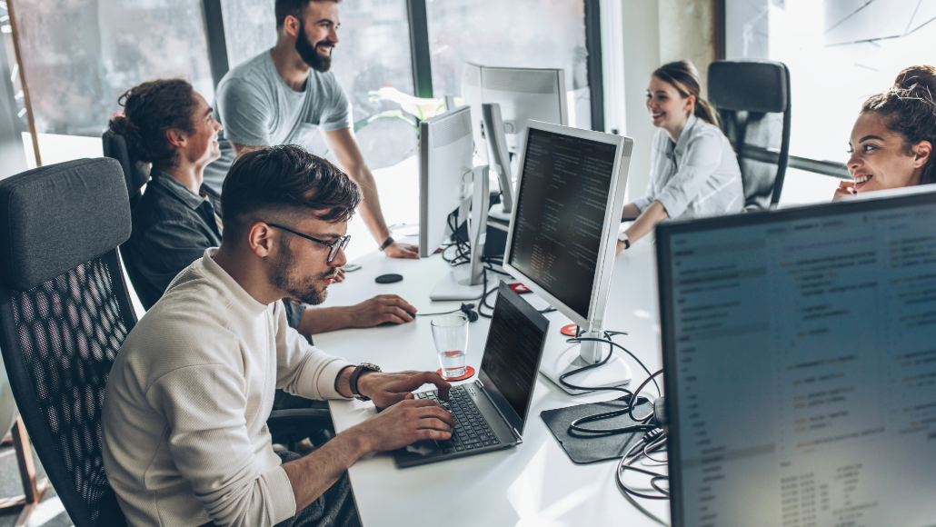 Software developer team working on computers while smiling and talking
