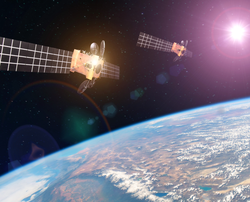 Two satellites orbiting the Earth with the sun reflected in the background